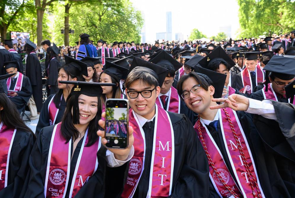 3 grads taking a selfie in front of full grad class