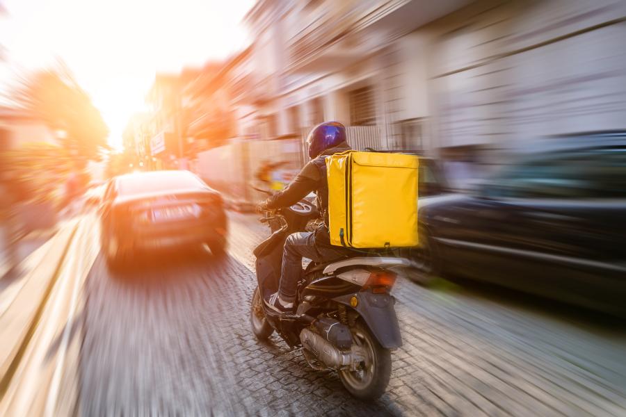 Delivery driver riding a scooter on a road, the image has a slight blur