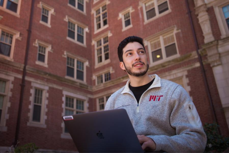 MIT student working on laptop in front of brick building