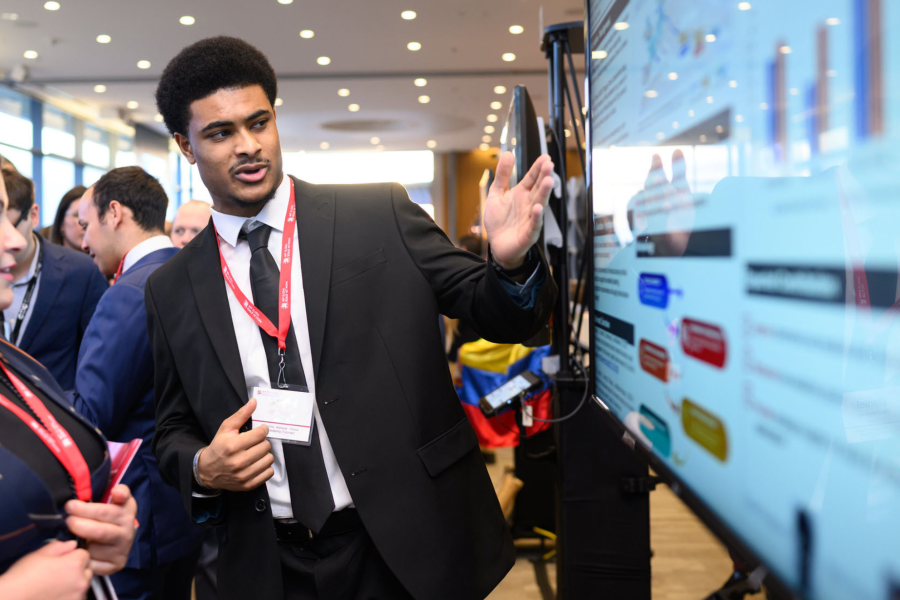Student in formal dress presenting research at a poster presentation